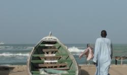 A boat on the sand by the ocean, and a person walking away
