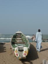 A boat on the sand by the ocean, and a person walking away